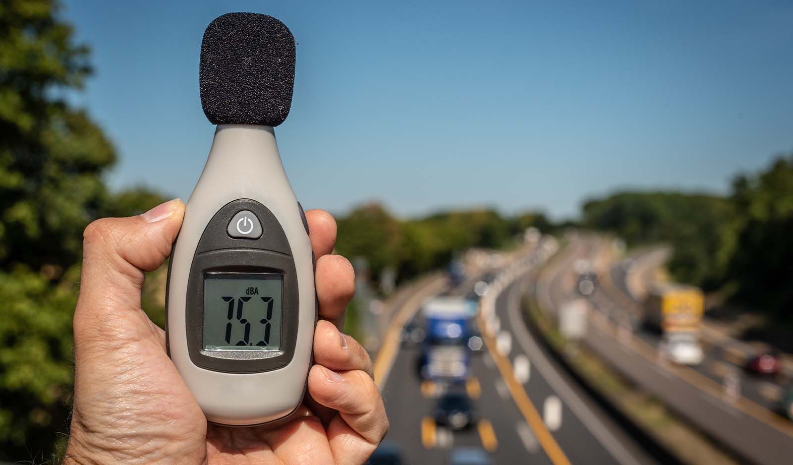 Hand holding a decibel meter to monitor traffic noise by a motorway